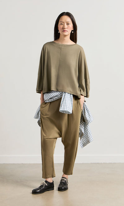Plümo- A woman in a Kaia Jersey boatneck top and loose khaki clothing stands against a plain light background.
