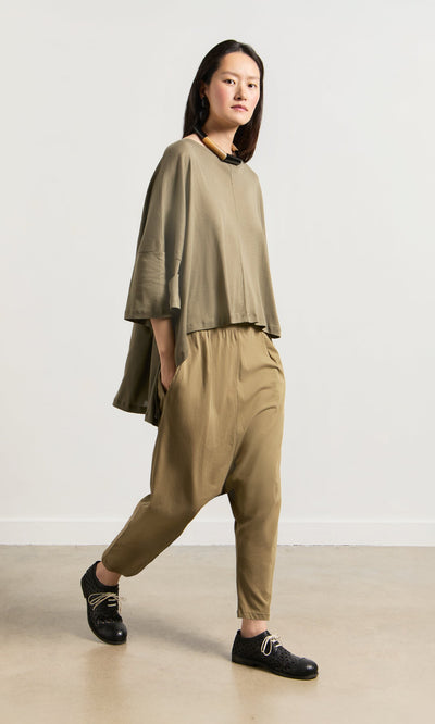 Plümo- A person in a drapey Kaia Jersey and black shoes walks indoors against a plain white wall.