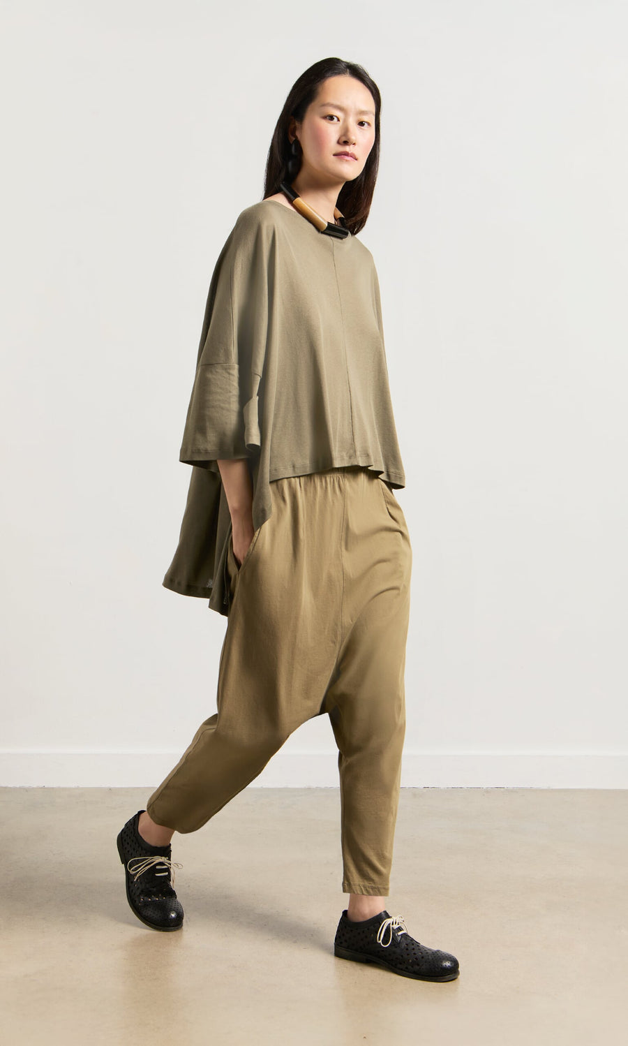 Plümo- A person in a drapey Kaia Jersey and black shoes walks indoors against a plain white wall.