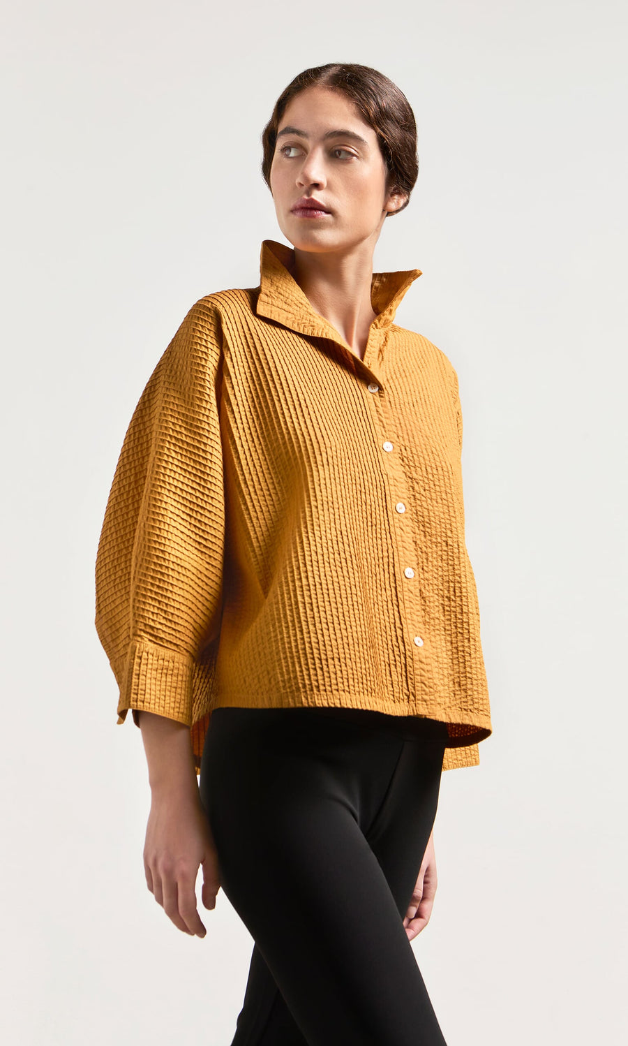 Plümo- Person in a textured mustard-yellow Karashi Shirt with black pants, looking to the side against a plain background.
