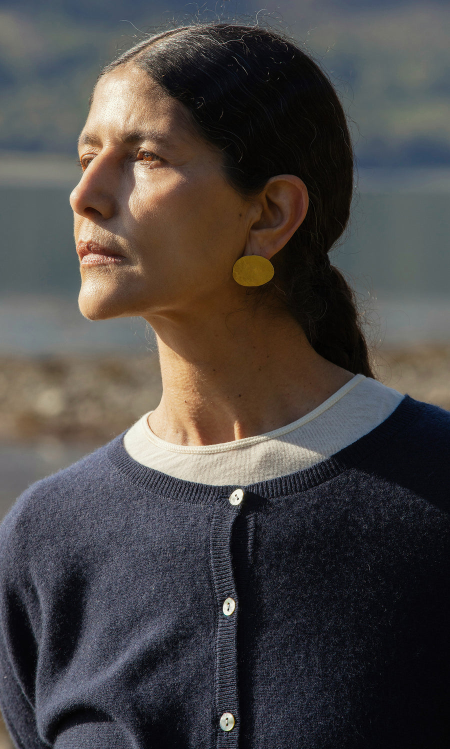 Plümo  Woman with dark hair in a ponytail, navy sweater, and Cohen Earrings looks thoughtfully to the side.