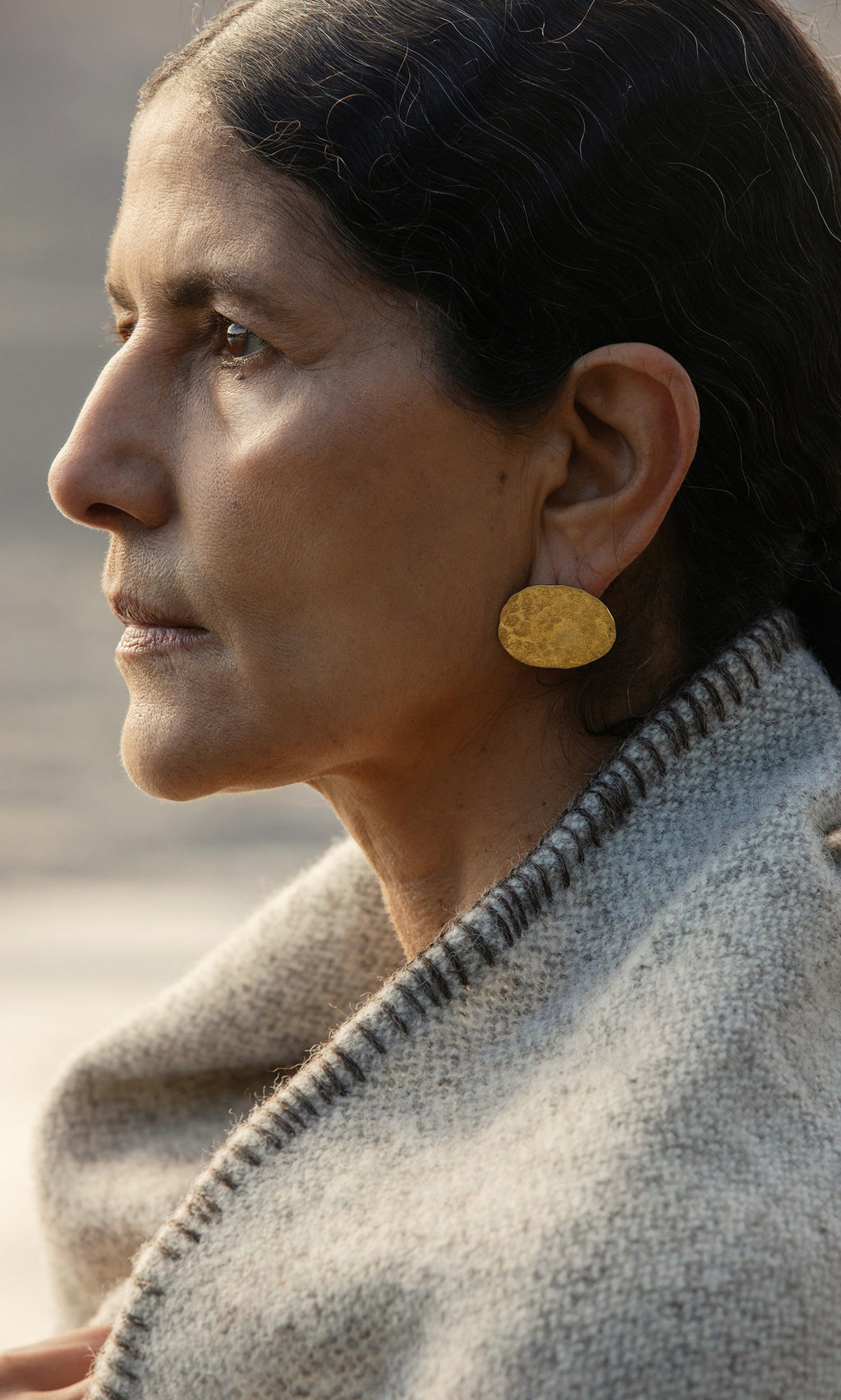 Plümo  A woman in profile wears the Cohen Earrings and a gray wool shawl, gazing thoughtfully into the distance.