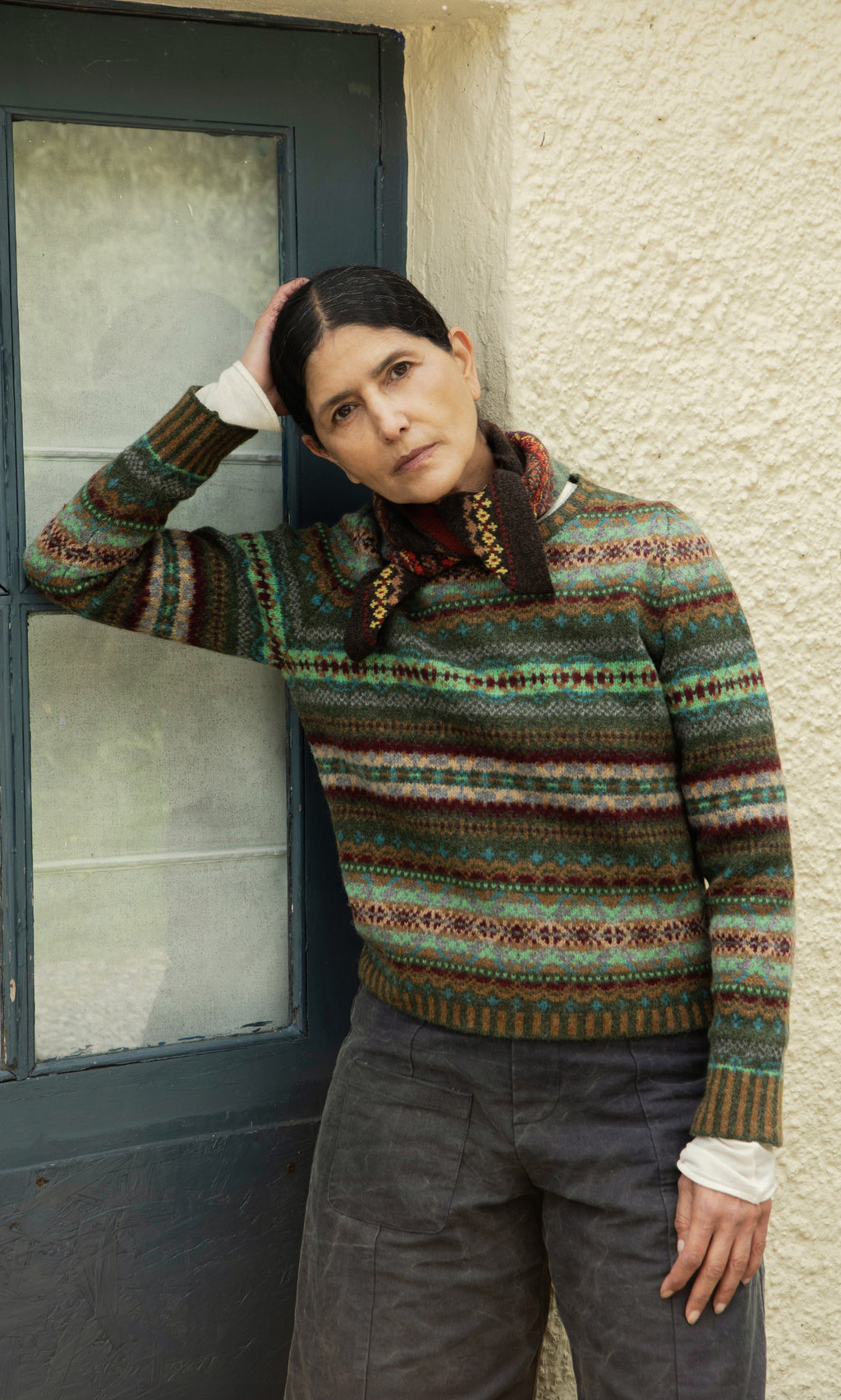 Plümo  Woman in a Lenie Necktie leans by a blue door, looking thoughtful—a touch of Scottish Borders style.