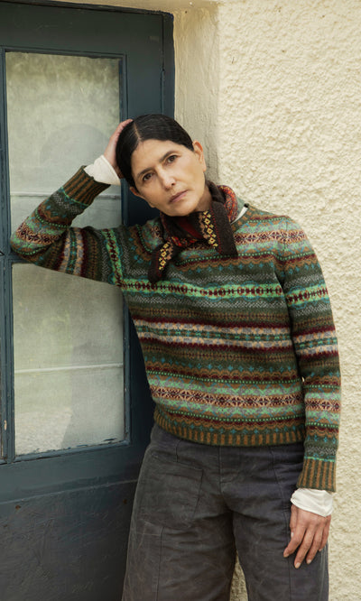 Plümo  Woman in a Lenie Necktie leans by a blue door, looking thoughtful—a touch of Scottish Borders style.