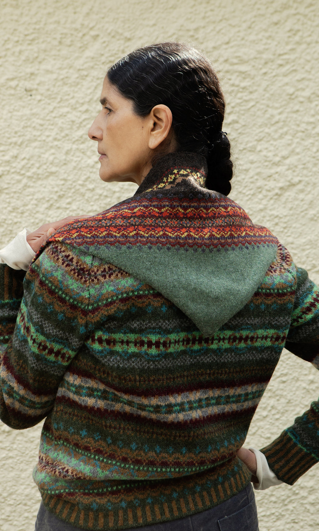 Plümo  Woman with dark braided hair wears the Lenie Necktie, facing a textured beige wall in the Scottish Borders.