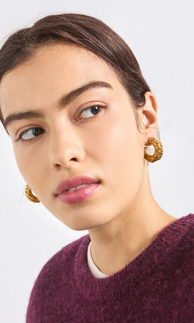 Plümo- A woman with slicked-back hair wears Lili Hoops and a plum sweater, gazing sideways against a plain background.