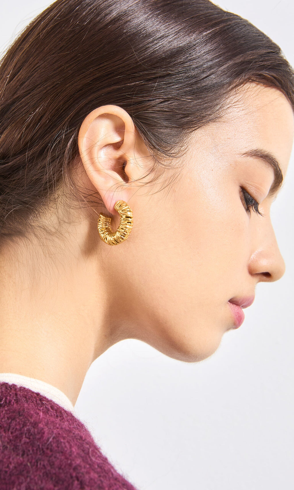Plümo- Woman with dark hair in profile wears Lili Hoops and a burgundy top against a plain background.