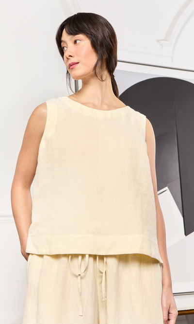 Plümo- Woman in the sleeveless, boxy Linda Top in Milk stands indoors with matching pants, looking to the side.