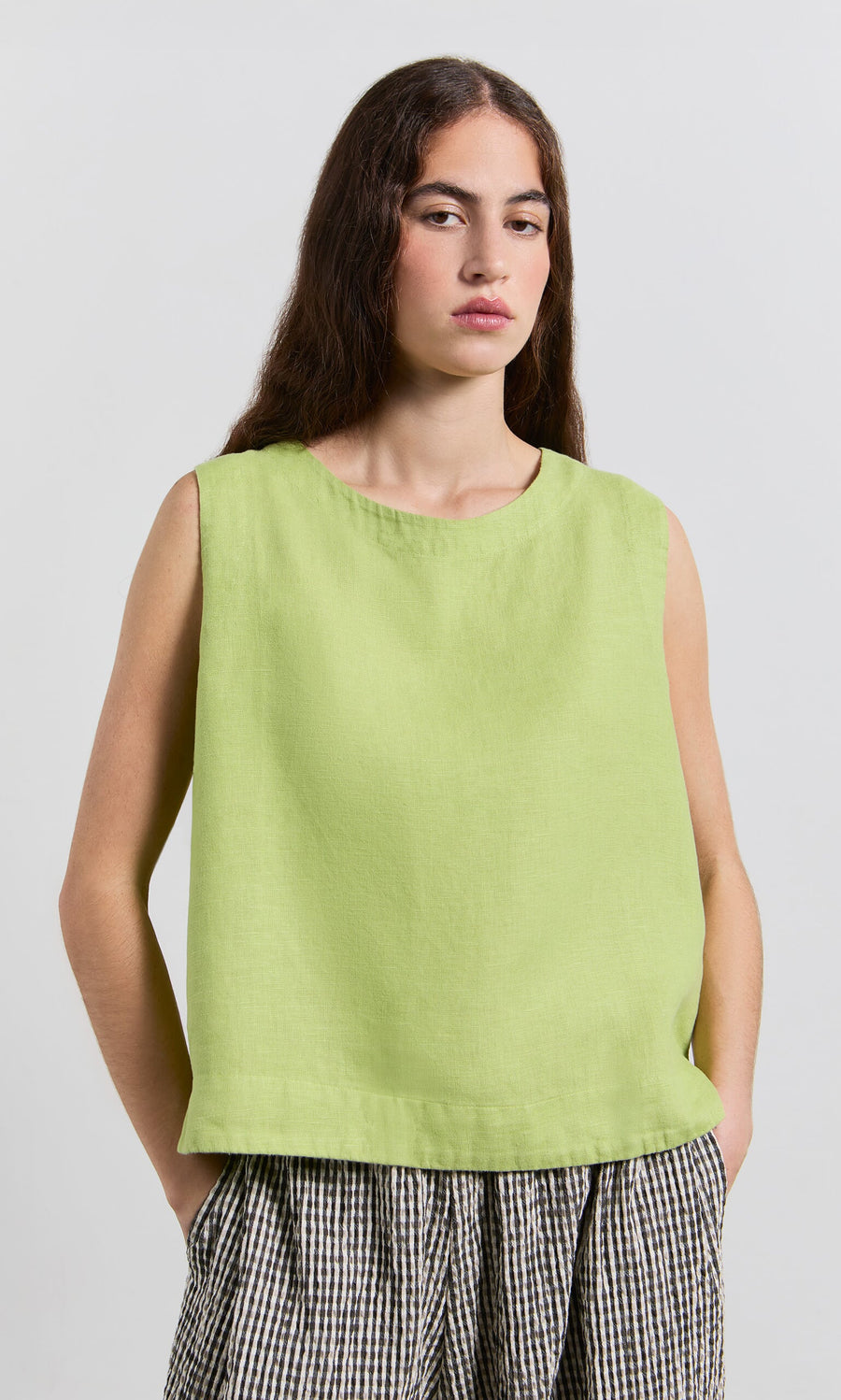 Plümo- Woman with long brown hair wears the Linda Top - Sorrel, a linen shell with scoop neck, and checked pants.