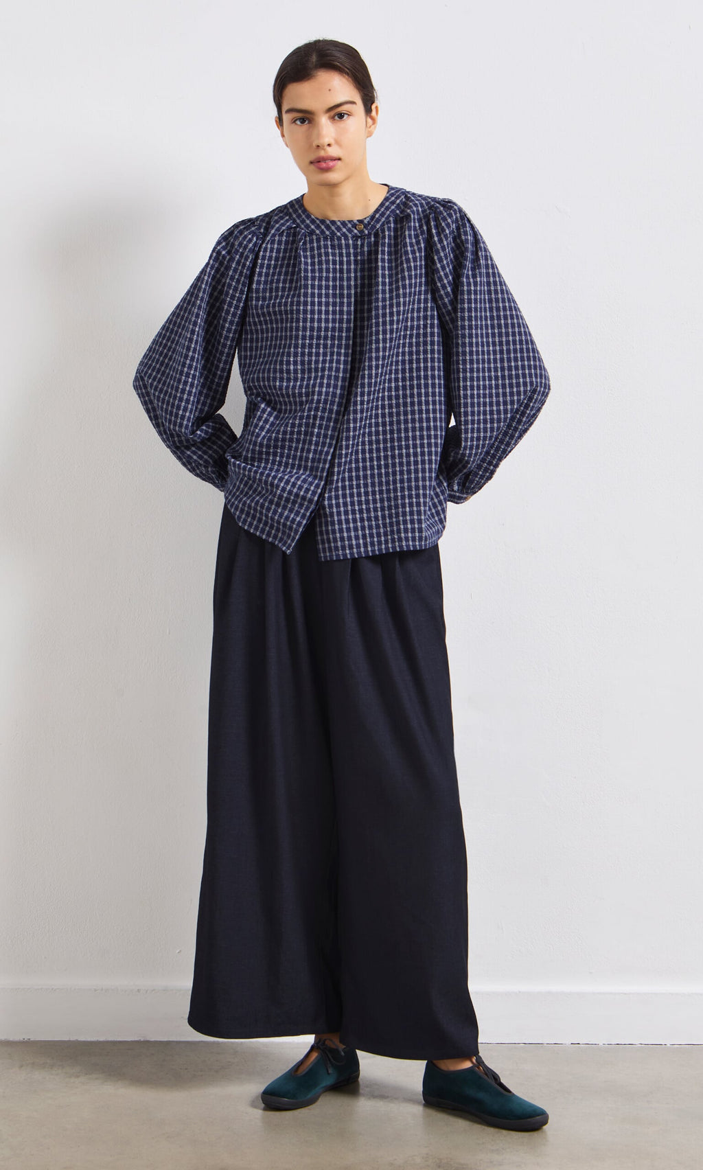 Plümo- Person wearing the Little Prairie Blouse, wide-leg dark pants, and dark shoes, standing against a white wall.