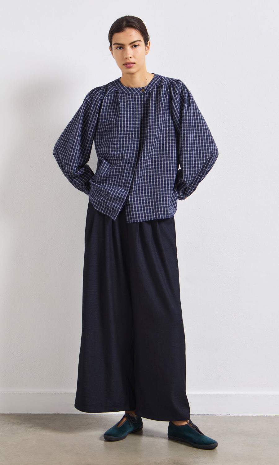 Plümo- Person wearing the Little Prairie Blouse, wide-leg dark pants, and dark shoes, standing against a white wall.