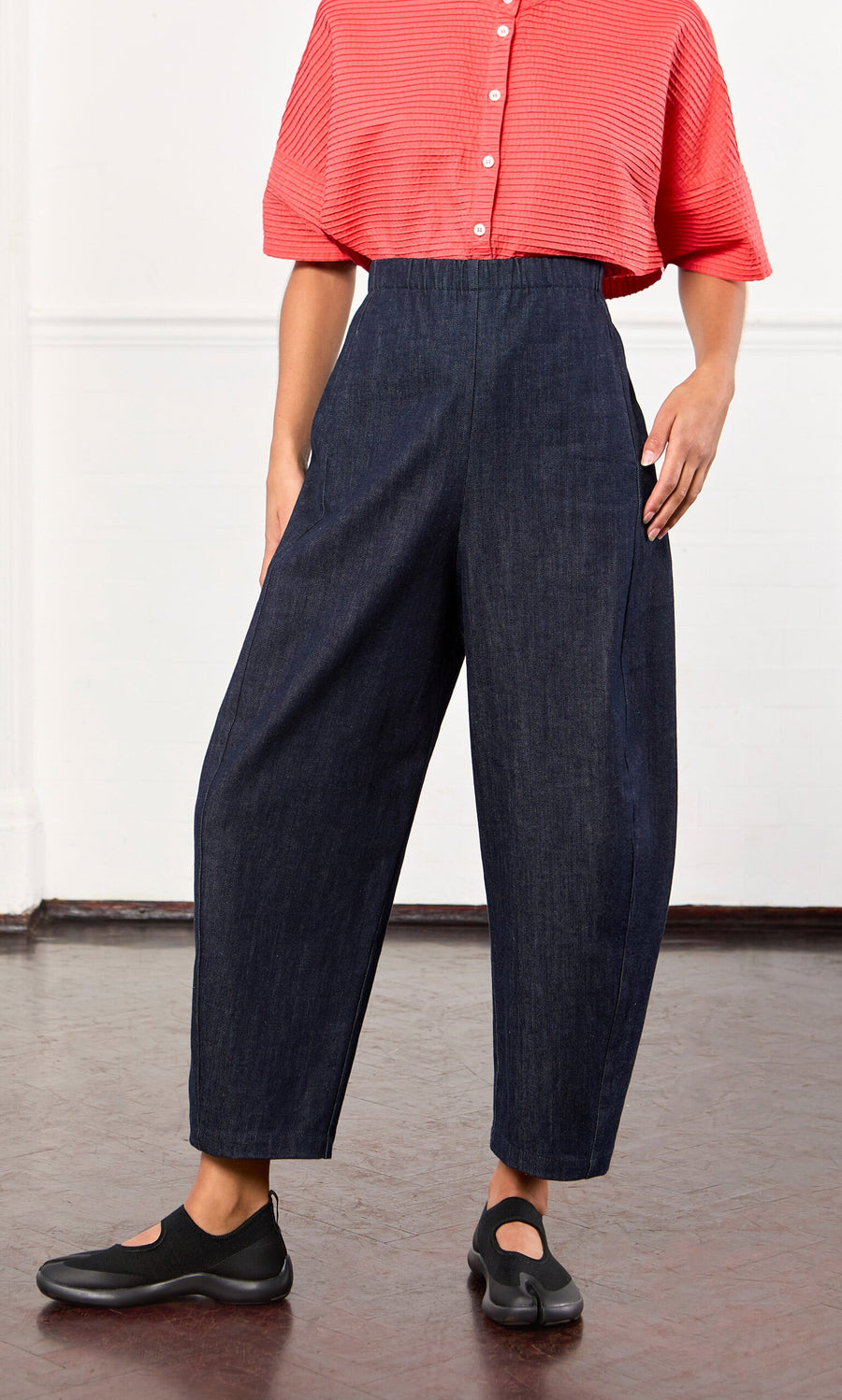 Plümo- Person in a red short-sleeve shirt and Lugo Barrel Jeans with elastic waist, standing indoors.