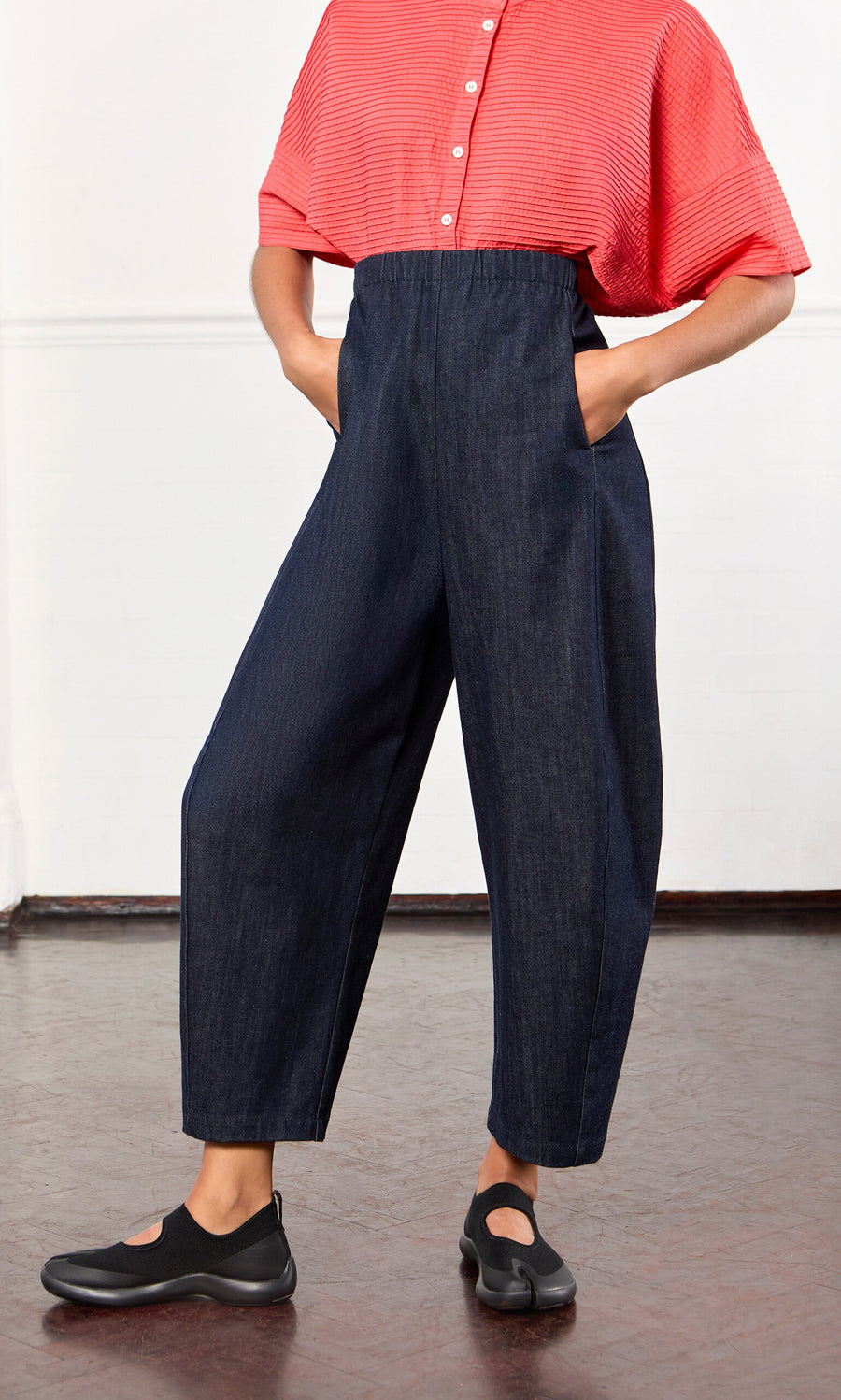 Plümo- Person in a red short-sleeve shirt and Lugo Barrel Jeans stands with hands in pockets.
