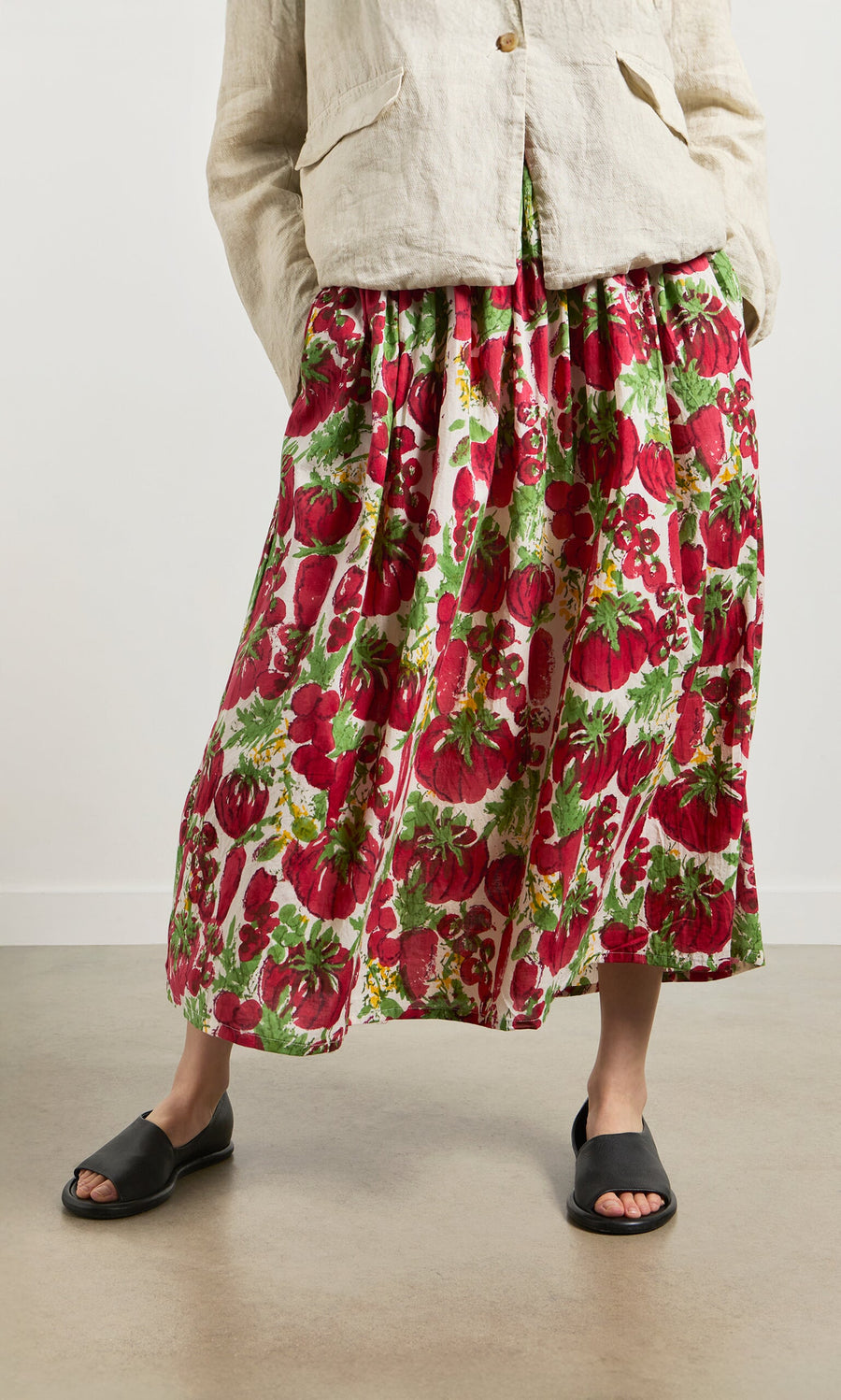 Plümo- Person wearing a beige jacket, Marzano Skirt, and black sandals, standing indoors.