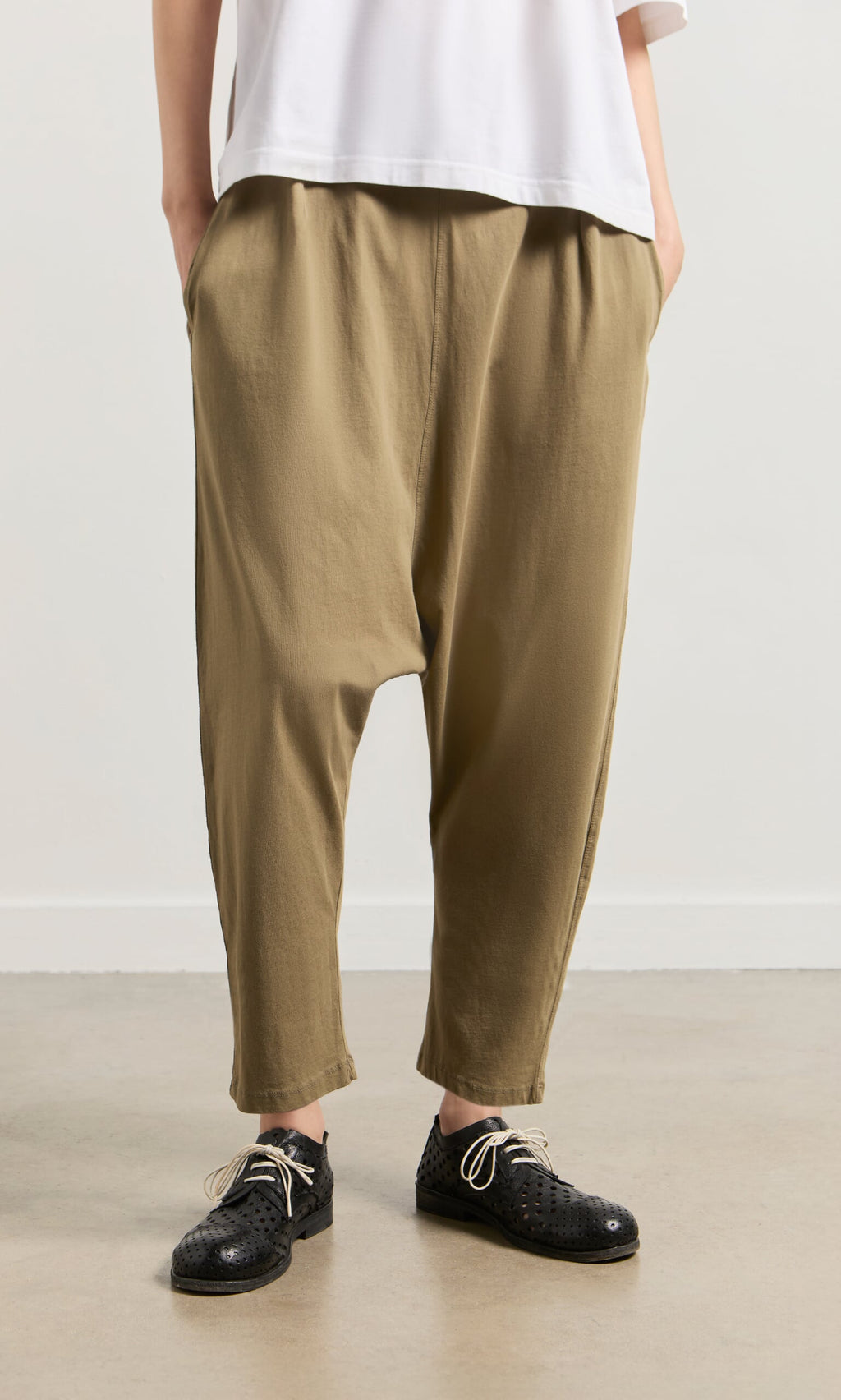Plümo- Person wearing Mirana Pants in tan, a white top, and black woven shoes, standing on a light-colored floor.