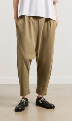 Plümo- Person wearing Mirana Pants in tan, a white top, and black woven shoes, standing on a light-colored floor.