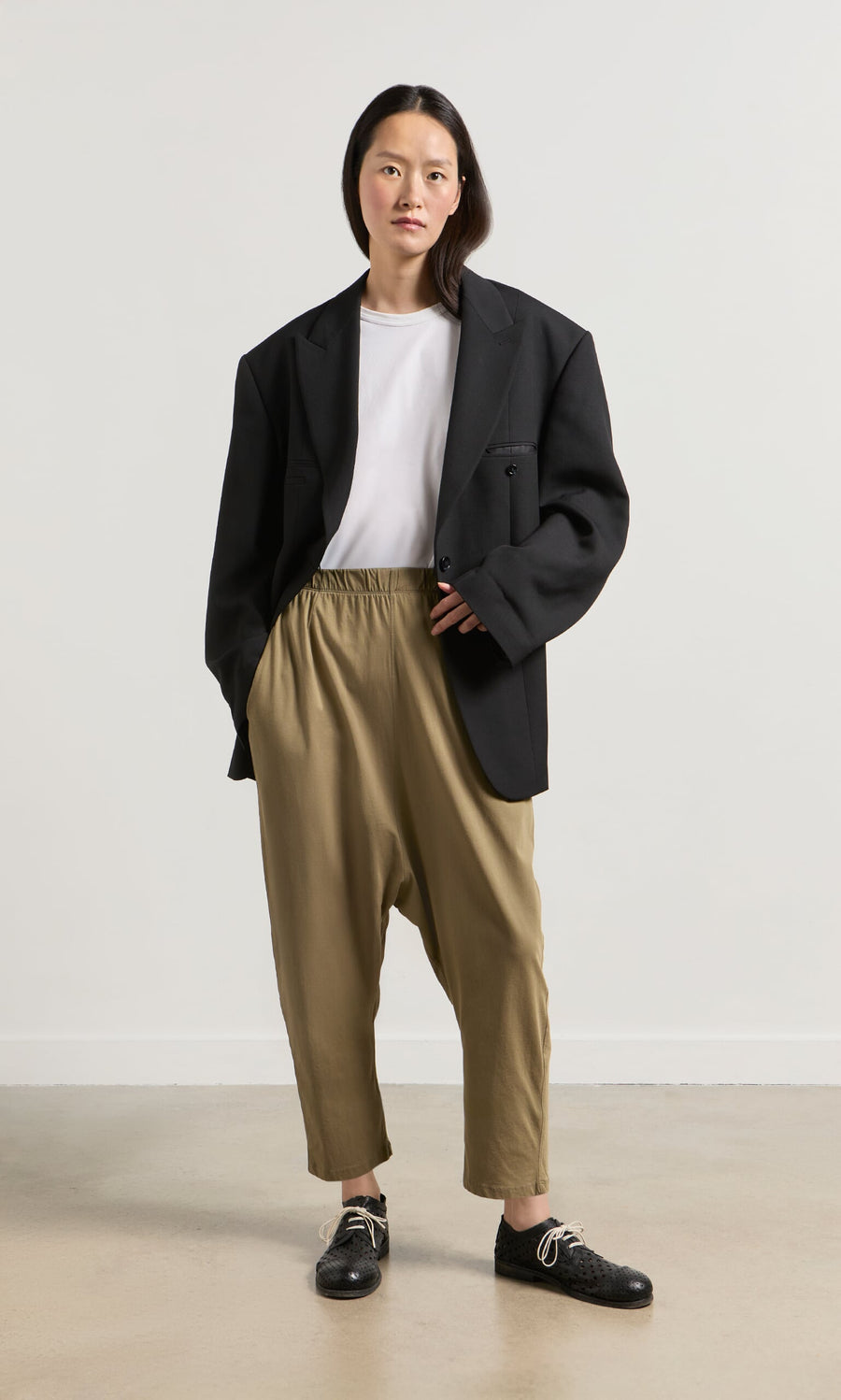 Plümo- Woman wears oversized black blazer, white tee, and Mirana Pants in classic Danish design against a plain background.