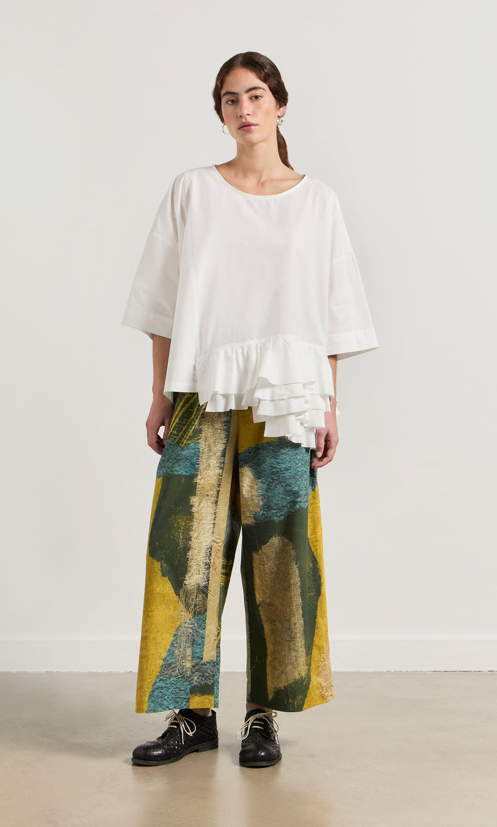 Plümo- Woman wears the Mirelle Blouse with wide-leg yellow and green abstract pants featuring an asymmetric hem.
