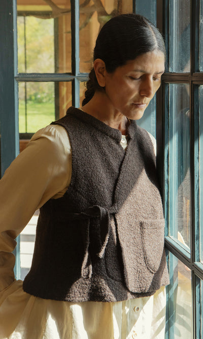 Plümo  A woman in a Mons Felted Waistcoat stands by the window, sunlight warming her thoughtful face.