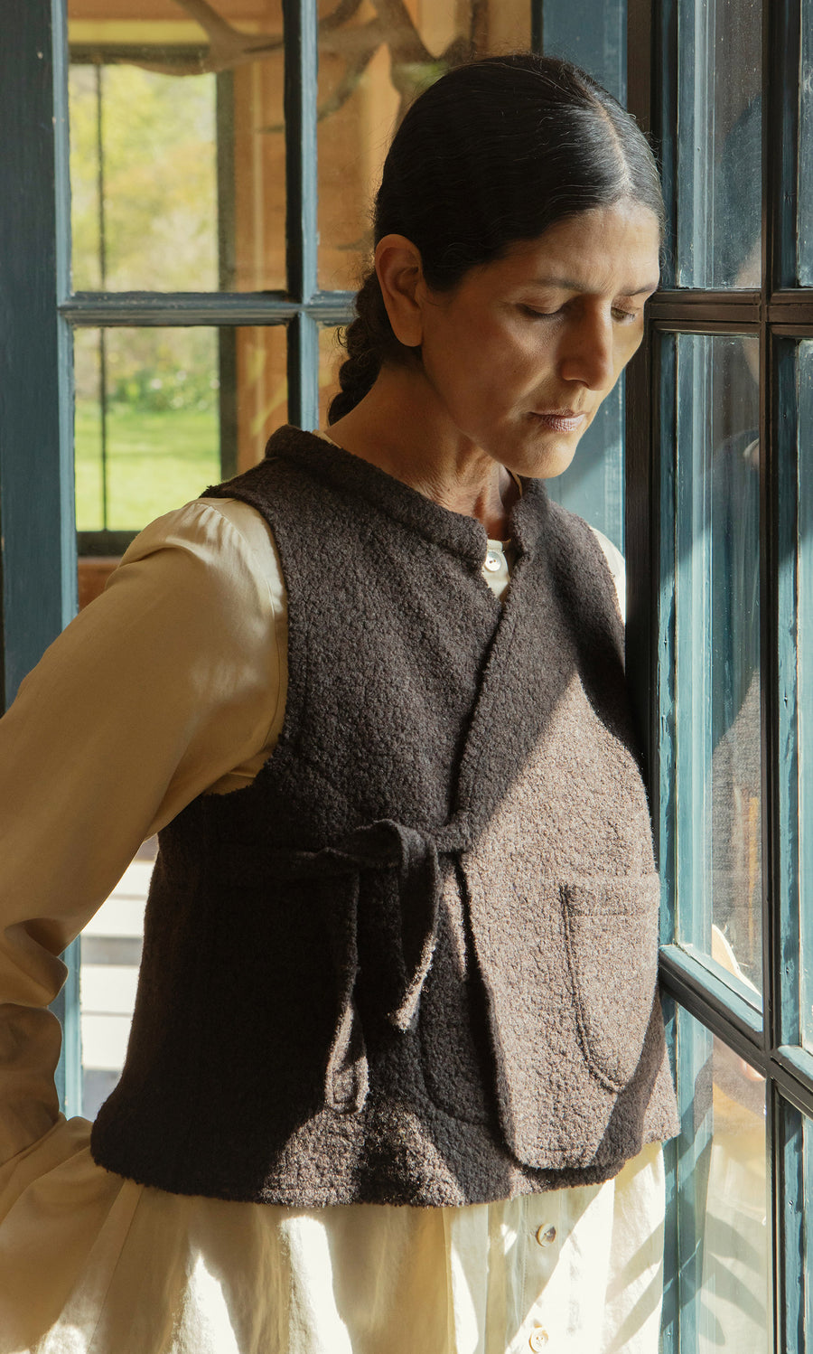 Plümo  A woman in a Mons Felted Waistcoat stands by the window, sunlight warming her thoughtful face.