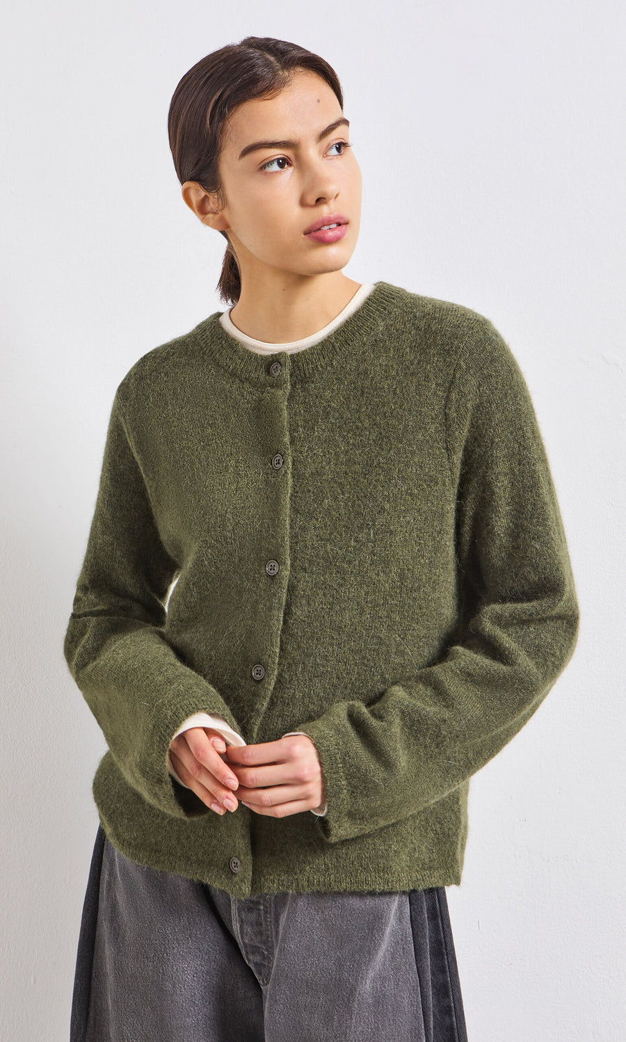 Plümo- Woman in an olive green cardigan over a white shirt, against a plain background.