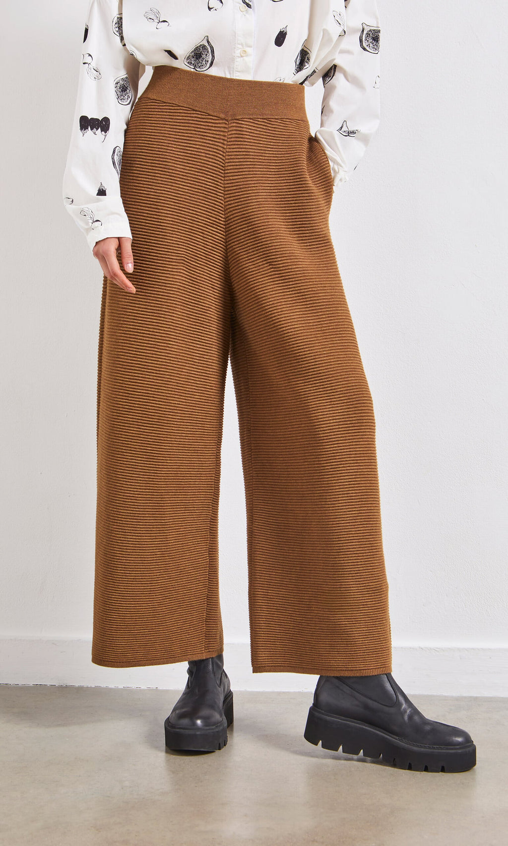 Plümo- Person wearing Orla Pants - Chestnut, black platform boots, and a patterned white shirt indoors.