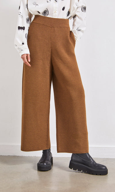Plümo- Person wearing Orla Pants - Chestnut, black platform boots, and a patterned white shirt indoors.