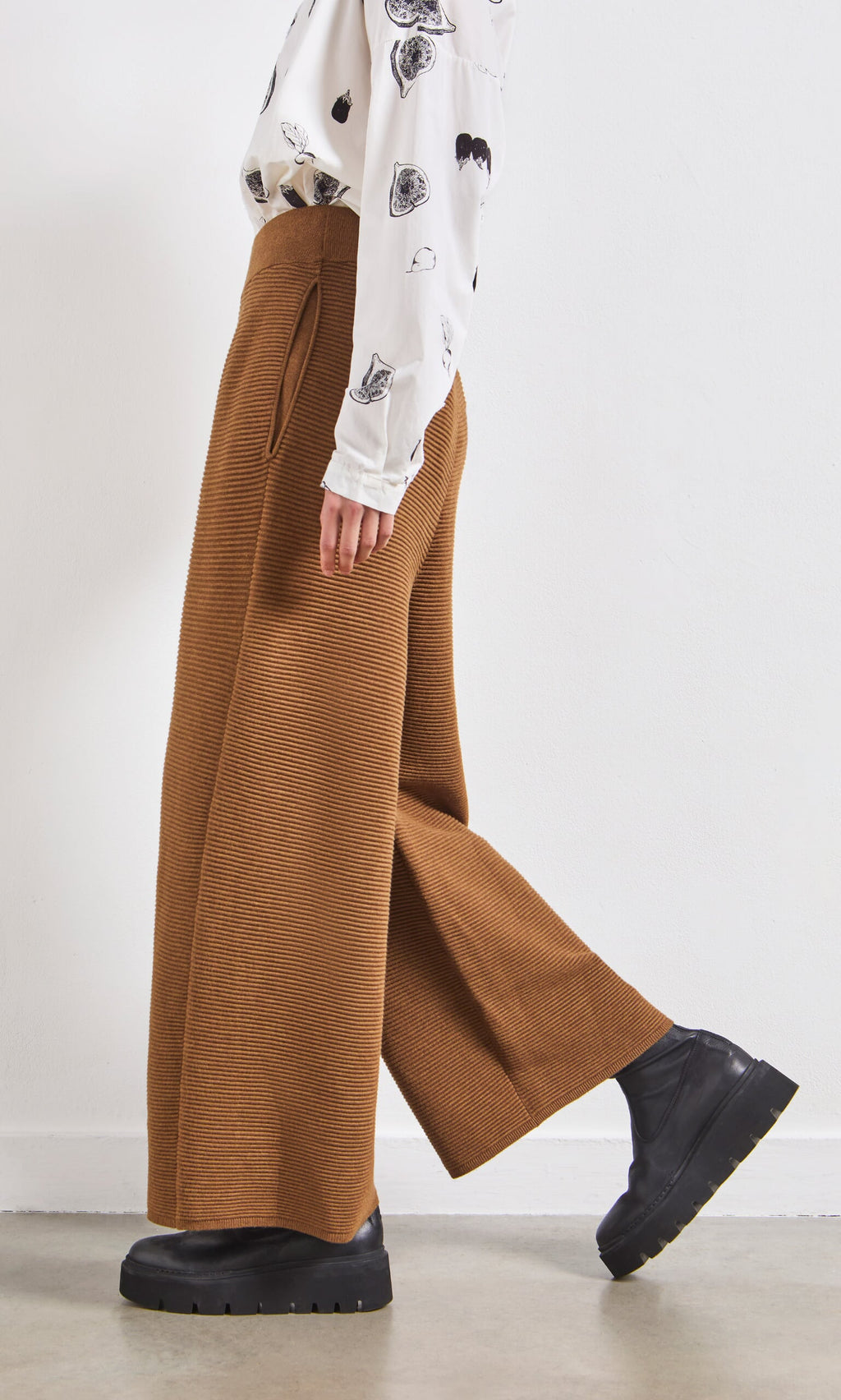 Plümo- Person wearing Orla Pants - Chestnut, black shoes, and a white patterned shirt stands against a plain background.
