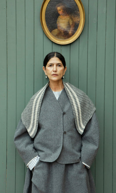 Plümo  Woman in gray coat and Oyster Triangle Scarf stands by green wall with child’s oval portrait above her head.
