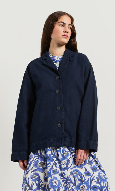 Plümo- Woman in a Maren Jacket over a blue and white floral dress, standing against a plain background.