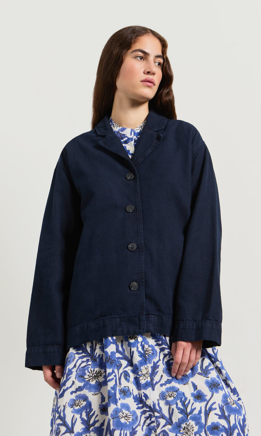 Plümo- Woman in a Maren Jacket over a blue and white floral dress, standing against a plain background.