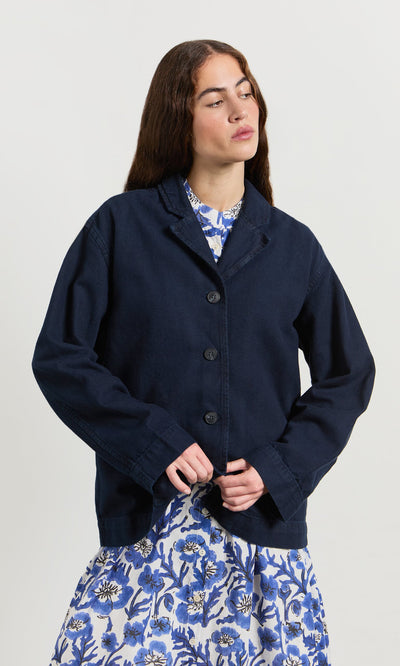 Plümo- A woman wears the Maren Jacket over a blue and white floral dress against a plain light background.