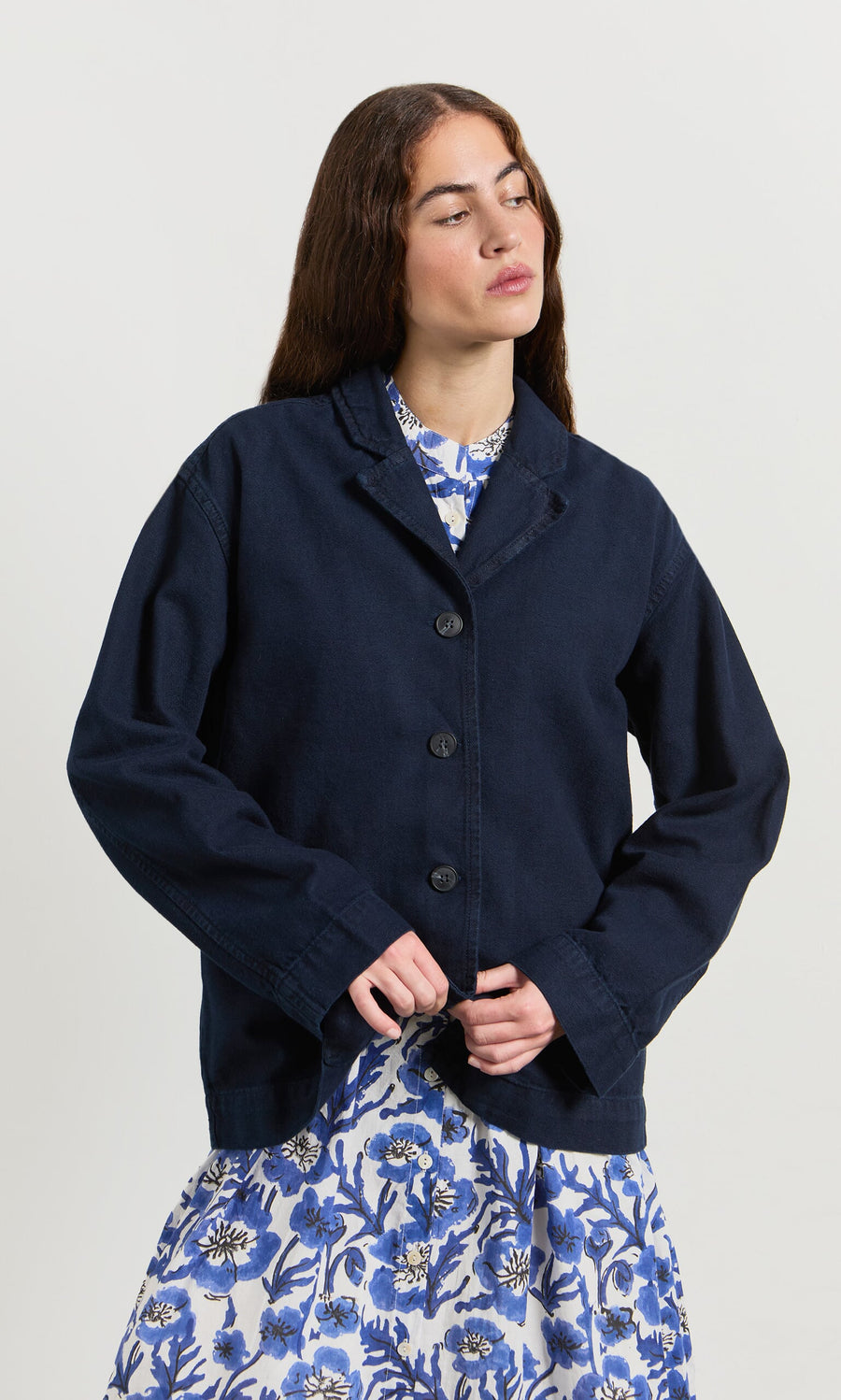 Plümo- A woman wears the Maren Jacket over a blue and white floral dress against a plain light background.