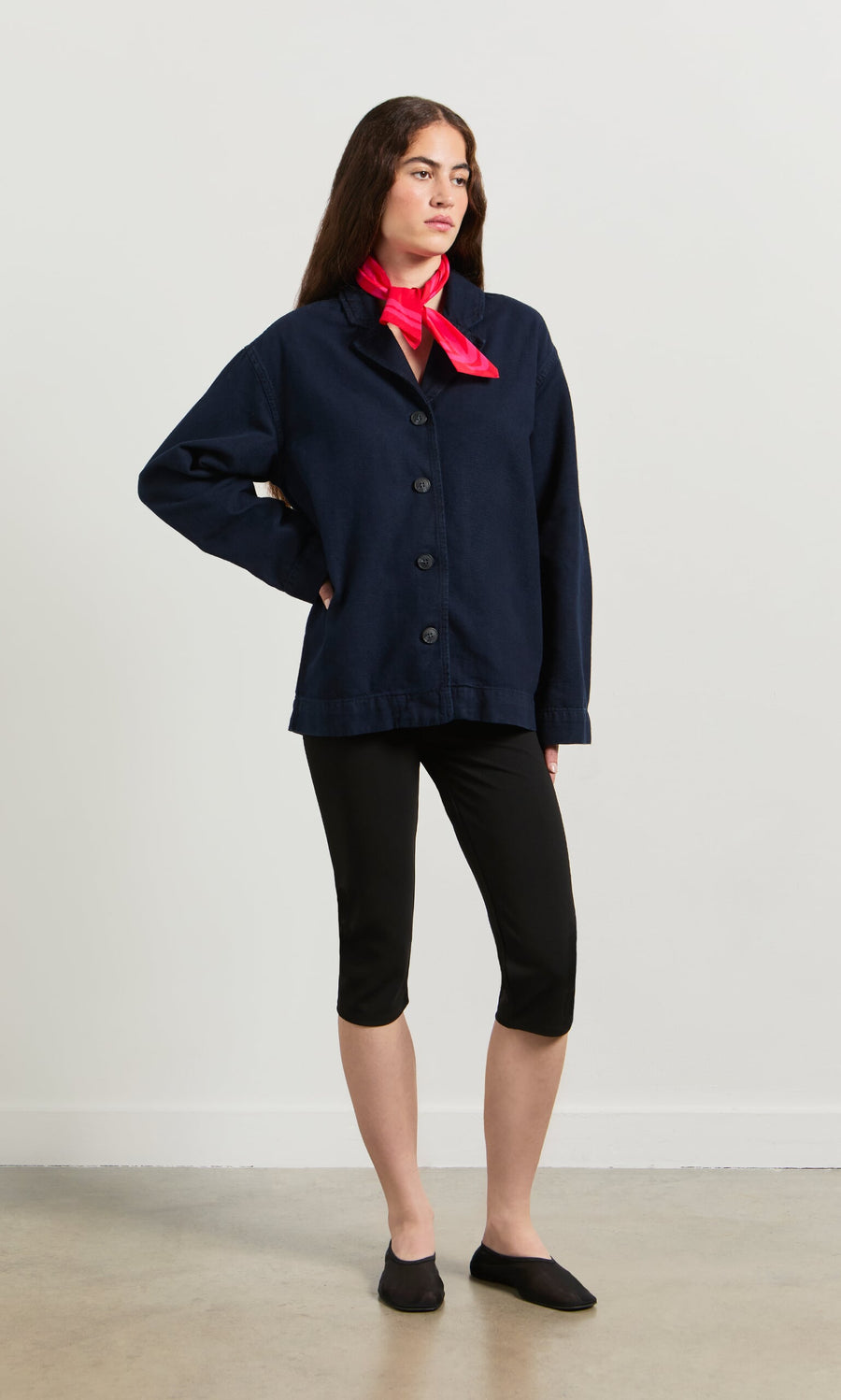 Plümo- Woman wears a navy Maren Jacket, black cropped leggings, and a bright pink scarf against a plain background.