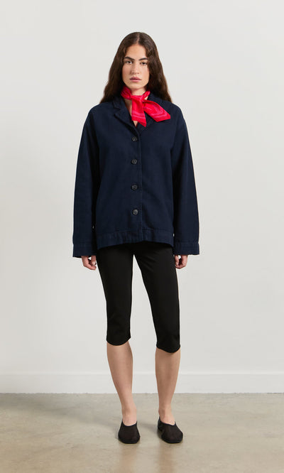 Plümo- A woman in a navy jacket, black capris, and flats wears the Poinsettia Necktie against a plain white wall.