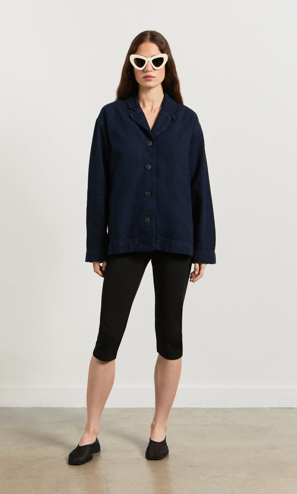 Plümo- A woman in white cat-eye sunglasses models the navy Maren Jacket against a plain background.