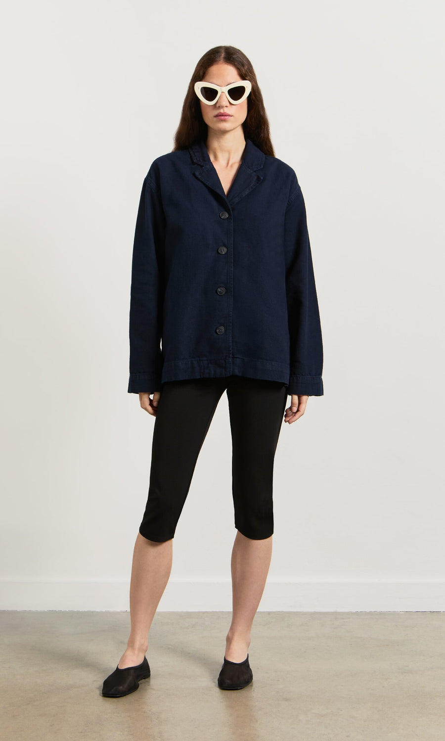 Plümo- A woman in white cat-eye sunglasses models the navy Maren Jacket against a plain background.