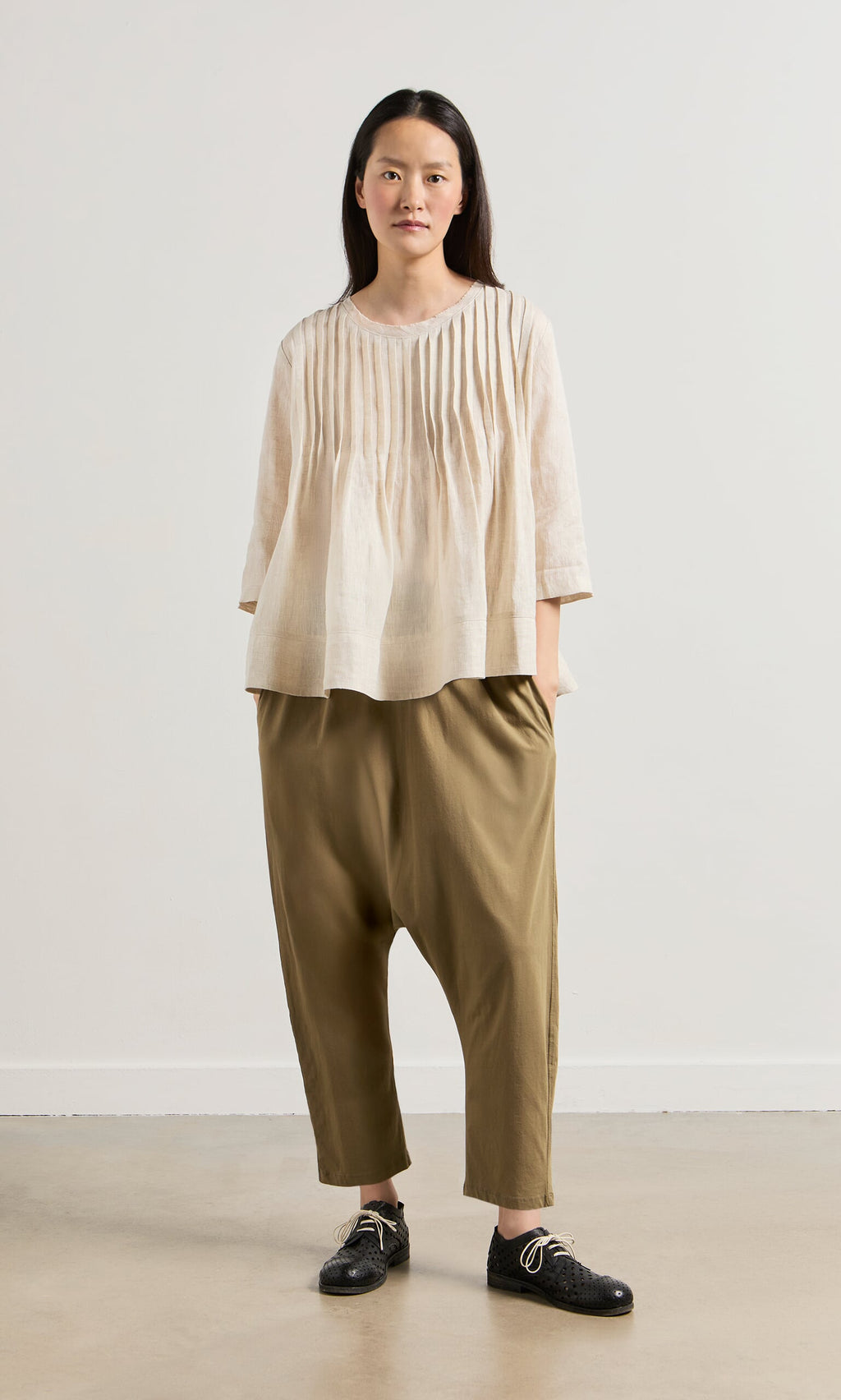 Plümo- Person wearing a relaxed fit ecru Pantry Blouse, olive harem pants, and black lace-up shoes against a plain background.