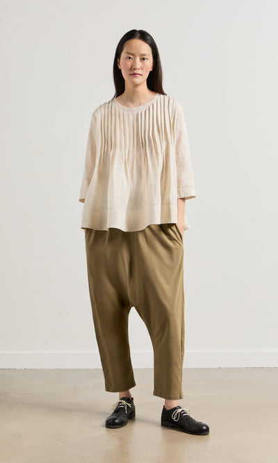 Plümo- Person wearing a relaxed fit ecru Pantry Blouse, olive harem pants, and black lace-up shoes against a plain background.