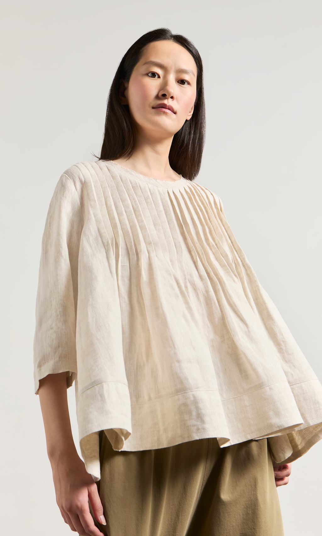 Plümo- Woman in a relaxed fit Pantry Blouse in ecru linen and olive green pants, standing against a plain background.