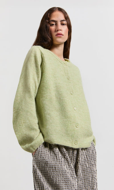 Plümo- Woman wears the Pistaz Cardigan, a light green crew neck, with checkered pants, hands in pockets.