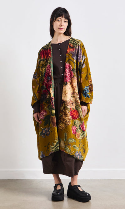 Plümo- A woman wears a brown dress, the Pomfret Kimono, and black platform shoes.