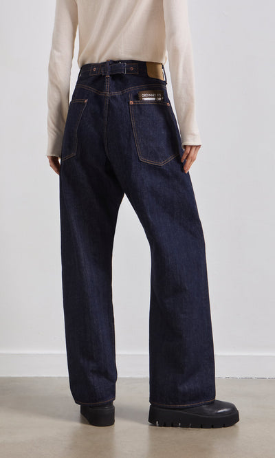 Plümo- Person wearing Japanese Raw Denim Jeans, cream long-sleeve top, and black shoes, standing against a plain wall.