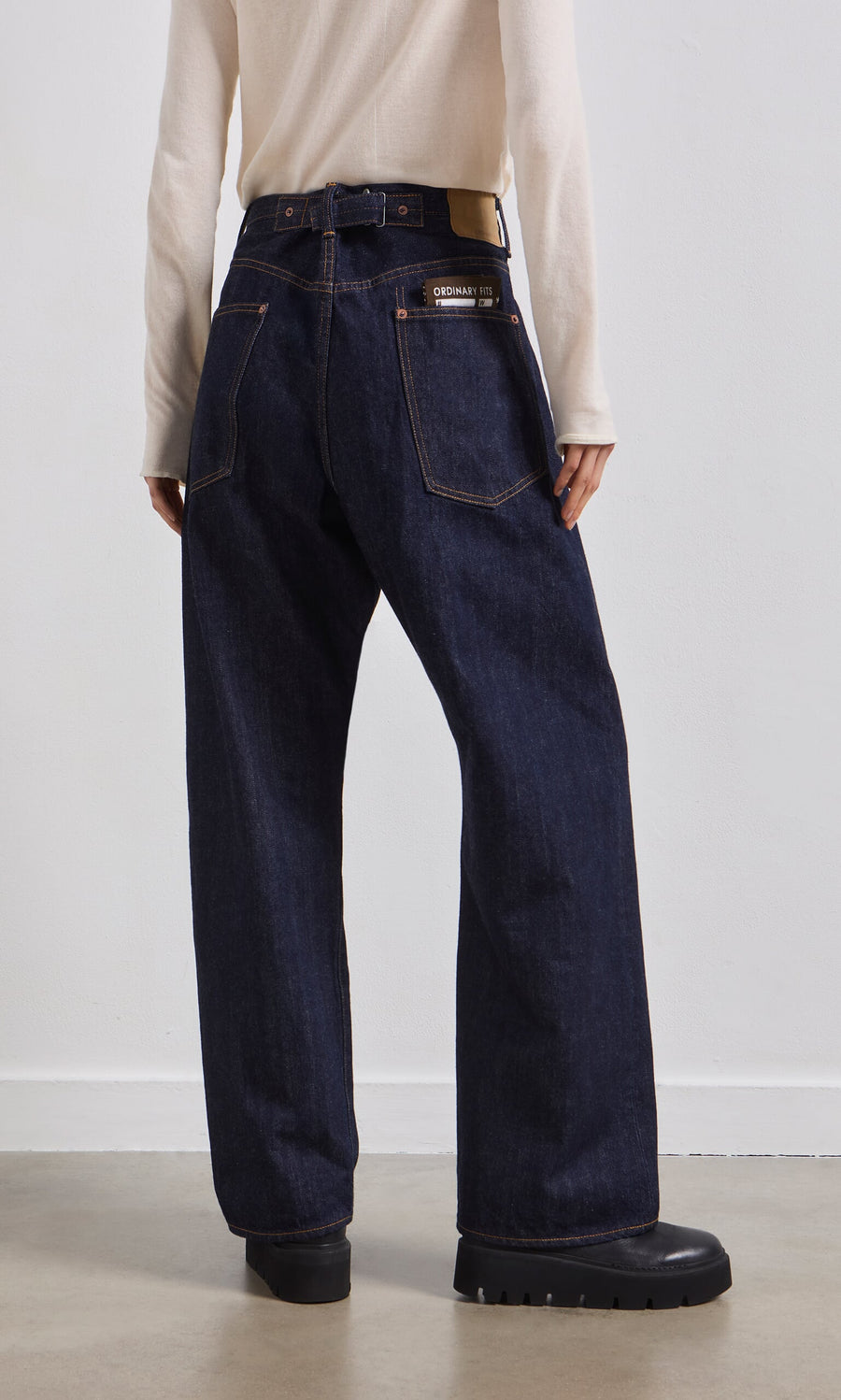 Plümo- Person wearing Japanese Raw Denim Jeans, cream long-sleeve top, and black shoes, standing against a plain wall.