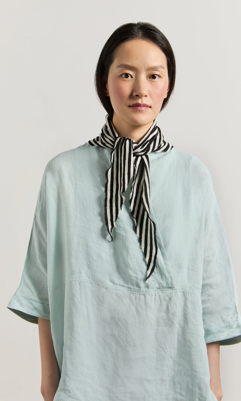 Plümo- Woman in a light blue top wears the Lynn Stripe Necktie, standing against a plain light background.