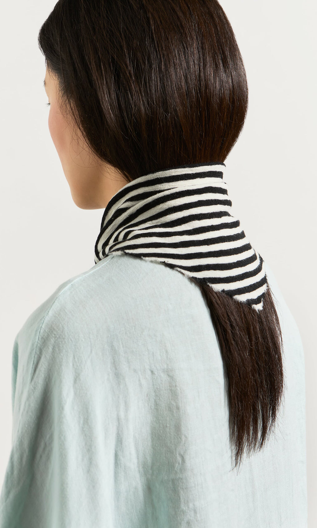 Plümo- Woman with straight brown hair in a light blue top, wearing the Lynn Stripe Necktie, viewed from behind.