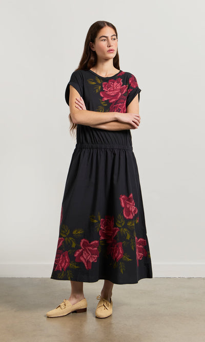 Plümo- Woman in the Rose Stitch Dress with large red florals and beige woven shoes featuring a cross-stitch rose design.