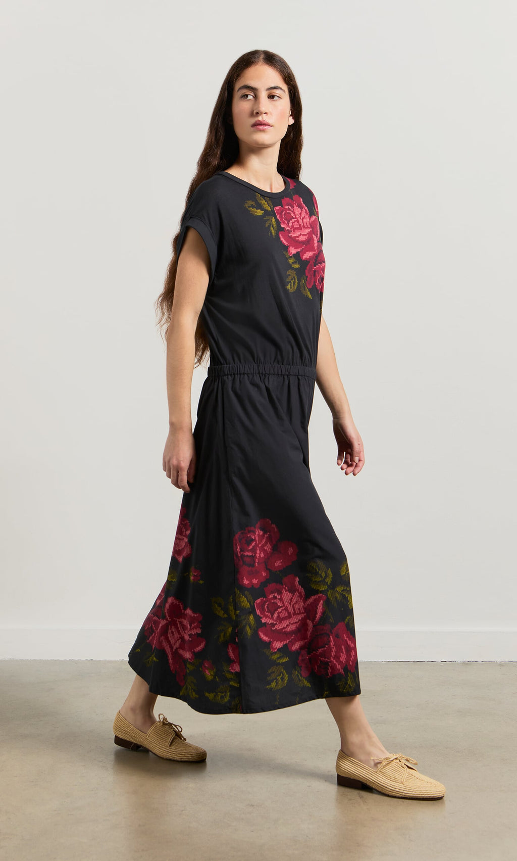 Plümo- Woman wears the Rose Stitch Dress and beige shoes, walking indoors on a light brown floor.