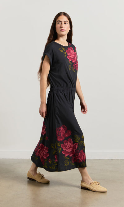 Plümo- Woman wears the Rose Stitch Dress and beige shoes, walking indoors on a light brown floor.