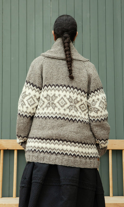 Plümo  Someone with a braid wears the Shingle Cardigan, standing back to the camera against a green wall.